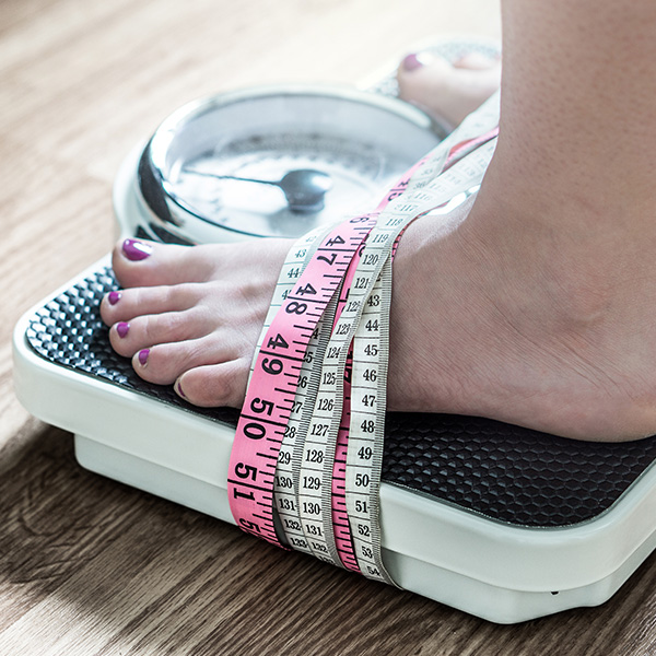 A person with their feet taped to the scale using measuring tape, symbolising feeling trapped by dieting